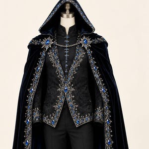 May include: A floor-length navy blue velvet hooded cloak featuring intricate gold embroidery and blue gemstone accents. The cloak is worn over a black patterned vest, a black button-up shirt, black trousers, and black dress shoes.