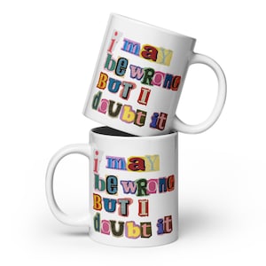 May include: Two white ceramic mugs stacked vertically. Each mug features the text "I may be wrong BUT I doubt it" printed in a ransom note style with letters in various colours and fonts, mimicking cut-out magazine clippings against the white surface.