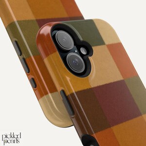 Peut inclure: Une coque de t&eacute;l&eacute;phone avec un motif &agrave; carreaux multicolore dans des tons orange, marron, beige et vert olive. La coque pr&eacute;sente une d&eacute;coupe noire pour l'appareil photo avec deux objectifs et un flash, ainsi que des boutons lat&eacute;raux noirs. Le texte Pickled Pearls est visible.