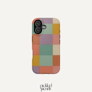 Puede incluir: Una funda de teléfono rectangular con un patrón de cuadrícula de cuadrados sólidos en tonos apagados de amarillo mostaza, verde salvia, rosa empolvado, lavanda y crema. La funda tiene un área negra para la cámara en la esquina superior.