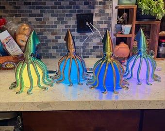 May include: Four squid-shaped lamps with iridescent, multi-coloured bodies and tentacles. Each lamp features a central glowing light source, with colours shifting between yellow, blue, and white, creating a vibrant display of light and shadow.