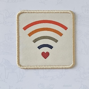 Puede incluir: Un parche termoadhesivo cuadrado con fondo crema y borde bordado en dorado. El diseño presenta un símbolo de Wi-Fi compuesto por cuatro líneas curvas en rojo, naranja, verde oliva y azul marino, con un pequeño corazón rojo centrado debajo.