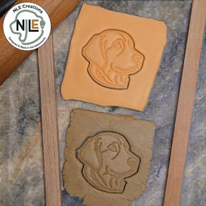 Op de afbeelding: Een lichtoranje vierkant stuk deeg en een donkerbruin vierkant stuk deeg, elk met een ingedrukte omtrek van een hondenkop. Een cirkelvormig logo in de linkerbovenhoek toont de tekst NLE Creations, NLE en Designed & Made in the Netherlands.