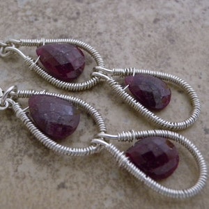 May include: A pair of silver wire wrapped earrings with teardrop shaped purple gemstones.