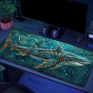 May include: A rectangular desk mat featuring a large shark illustration with intricate gold and teal filigree patterns. The shark is depicted swimming through deep teal water with swirling abstract designs and bubbles surrounding its body.