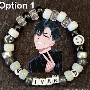 May include: A circular beaded bracelet featuring a central rectangular charm depicting an anime character with black hair making a peace sign. The bracelet is composed of alternating black, white, and translucent beads, including smiley face beads and letter beads spelling IVAN.