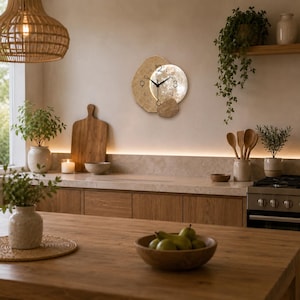 May include: A circular wall clock featuring a textured, gold-toned, irregular layered background and a central moon-like face with black numerals at the 3, 6, 9, and 12 positions, complemented by thin black hour, minute, and second hands.