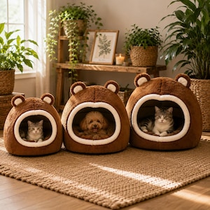 Pode incluir: Três camas de pelúcia castanhas para animais de estimação em forma de cabeça de urso com orelhas arredondadas e rebordo branco à volta das aberturas. Cada cama tem uma textura macia e felpuda. Duas camas contêm gatos tigrados e a central um cão pequeno de pelo encaracolado.