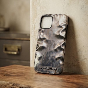 May include: A phone case with a metallic, rippled, and distressed surface texture in shades of dark grey and silver. The case features a rectangular camera cutout and the text "Be undefined" embossed in a serif font at the bottom centre.
