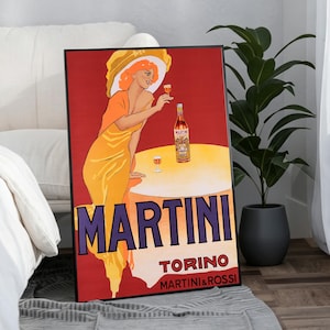 Può includere: Un poster incorniciato in stile vintage raffigurante una donna con un abito giallo e un cappello a tesa larga che tiene un bicchiere accanto a una bottiglia di Martini su un tavolo. Lo sfondo è rosso con il testo MARTINI TORINO MARTINI & ROSSI.