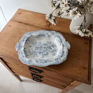 May include: A rectangular ceramic serving dish with scalloped edges and integrated side handles. The white surface features a detailed blue floral transferware pattern with roses and foliage covering the centre and the wide rim.