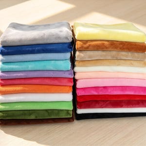 Könnte beinhalten: Zwei Stapel gefalteter rechteckiger Stoffstücke in einer Vielzahl von Unifarben, darunter Grau, Blau, Türkis, Lila, Rot, Orange, Weiß, Grün, Braun, Gelb, Beige, Creme, Pink, Magenta und Schwarz mit einer weichen, plüschigen Textur.