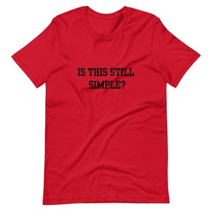 May include: Red short-sleeved t-shirt with black text that reads "IS THIS STILL SIMPLE?"