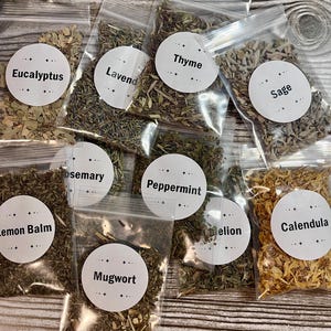 May include: A collection of nine clear plastic resealable bags filled with dried herbs, each featuring a white circular label with black text. The labels are labeled Eucalyptus, Lavender, Thyme, Sage, Rosemary, Peppermint, Dandelion, Lemon Balm, and Mugwort.