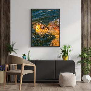 May include: A framed wall art print featuring a sea turtle with a textured, golden-brown shell and head surfacing from deep blue, rippling water. The turtle is captured in profile, showing its dark eye and mottled skin pattern above the water line.