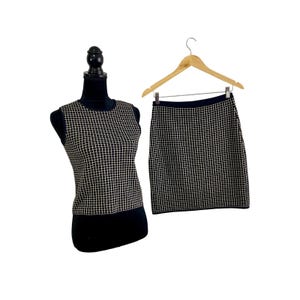 May include: A sleeveless top and a matching skirt, both featuring a black base with a white grid pattern. The top is displayed on a black mannequin, while the skirt is suspended from a wooden hanger with silver metal clips.