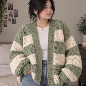May include: A chunky crochet cardigan featuring wide horizontal stripes in sage green and cream. The garment has an open front design, long sleeves with ribbed cuffs, and a thick ribbed border along the neckline and front opening.