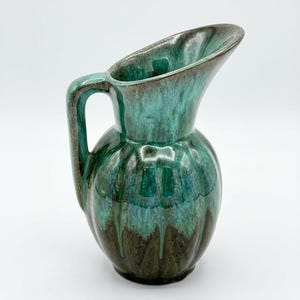 May include: A ceramic pitcher featuring a glossy glaze with a color gradient transitioning from a deep dark brown at the base to a vibrant turquoise and teal at the top. The vessel has a rounded body with vertical fluting and a curved handle.