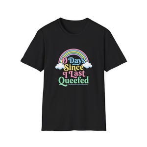 May include: A black short-sleeved t-shirt featuring a graphic print of a colorful rainbow with white clouds at the base. The text "0 Days Since I Last Queefed" is printed in a multi-colored, rounded font centered below the rainbow design.