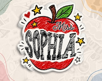 May include: A die-cut sticker shaped like a red apple with a green leaf and brown stem. The apple features the text Miss SOPHIA in black, scribbled-style lettering. The design is accented with small yellow stars and a red heart, all outlined in white.