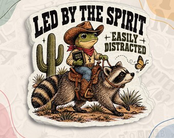 May include: A die-cut sticker featuring a green frog wearing a cowboy hat, red bandana, and shirt, holding a Holy Bible while riding a raccoon. The text reads LED BY THE SPIRIT EASILY DISTRACTED. A cactus and butterfly are visible.