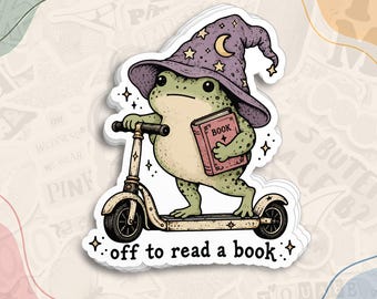 May include: A die-cut sticker featuring a green frog wearing a purple wizard hat with stars and a crescent moon. The frog is riding a scooter while holding a red book labeled BOOK. The text below reads off to read a book.