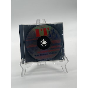 Puede incluir: Una caja de CD de plástico transparente que contiene un disco con la etiqueta IT, The Computer Games Quarterly, With Windows 95 Stuff. El disco presenta texto en rojo y azul sobre un fondo oscuro, sostenido por un soporte de acrílico.