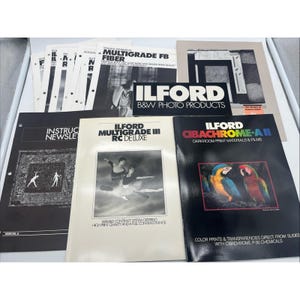 May include: A collection of Ilford technical information booklets and product brochures for darkroom photography. The documents feature black and white imagery, including ballet dancers and parrots, with text labels such as Multigrade FB Fiber, RC Deluxe, and Cibachrome-A II.