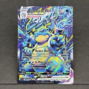 May include: A Blastoise VMAX trading card featuring a blue turtle character with water cannons, 320 HP, and attacks named Hydro Blaster and G-Max Geyser. The card has a vibrant, colorful graffiti-style background with blue, yellow, and purple accents.