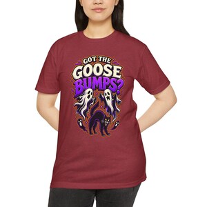 May include: A maroon short-sleeve t-shirt featuring a graphic print with the text "GOT THE GOOSE BUMPS?" in white and purple. The design includes two white ghosts and a black arched cat with glowing eyes, surrounded by small purple stars.