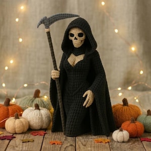 Könnte beinhalten: Eine gehäkelte Sensenmann-Figur mit beigem Totenkopfgesicht und Händen, die einen schwarzen Kapuzenumhang trägt und einen langen Stab mit einer grauen Sensenklinge hält, umgeben von mehreren kleinen, bunten gehäkelten Kürbissen.