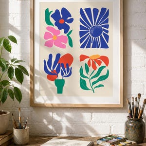 Peut inclure: Une impression d'art encadrée présentant quatre sections distinctes d'illustrations florales abstraites. L'œuvre affiche des formes audacieuses en bleu, rose, rouge, vert et orange sur un fond crème clair, dans un cadre en bois clair.