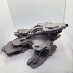 Peut inclure: Une sculpture de formation rocheuse grise imprimée en 3D présentant plusieurs plateaux plats superposés avec des lignes de contour horizontales visibles sur les surfaces. La structure a une forme organique irrégulière avec des sections creuses.