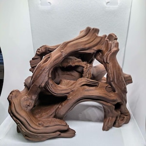 May include: A brown, textured piece of driftwood with a complex, gnarled structure featuring multiple twisted branches, deep grooves, and natural hollows. The wood has a matte finish and an intricate, organic shape with several open arches.