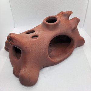 Könnte beinhalten: Eine terrakottafarbene, 3D-gedruckte Hohlstruktur mit glatter, matter Oberfläche. Das Objekt weist mehrere kreisförmige Öffnungen unterschiedlicher Größe an der Oberseite und den Seiten auf, mit einer geschichteten Textur, die für additive Fertigung typisch ist.