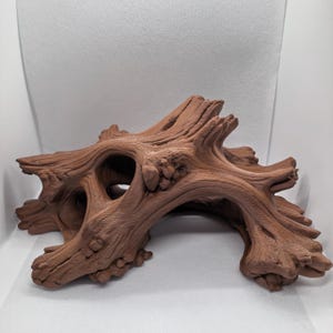 May include: A brown, textured, hollow piece of driftwood decor featuring intricate wood grain patterns, knots, and multiple openings. This organic-shaped structure mimics the appearance of a weathered tree root or branch with a matte finish.