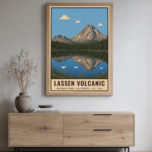 K&ouml;nnte beinhalten: Ein gerahmter Wandkunstdruck mit einer Landschaftsillustration des Lassen Volcanic Nationalparks in Kalifornien. Das Bild zeigt einen Berggipfel, der sich in einem See spiegelt, mit blauem Himmel, Wolken und dem Text LASSEN VOLCANIC NATIONAL PARK.