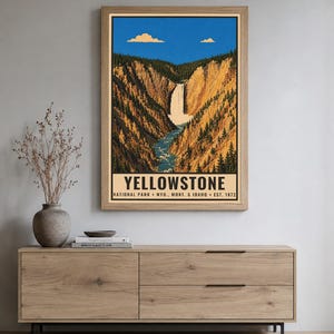 Op de afbeelding: Een verticale wandkunstprint met een landschapsillustratie van een waterval die door een kloof met dennenbomen stroomt, onder een blauwe lucht met twee wolken. De tekst luidt YELLOWSTONE NATIONAL PARK WYO., MONT. & IDAHO EST. 1872.