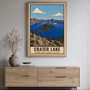 Może przedstawiać: Pionowy wydruk ścienny przedstawiający stylizowaną ilustrację Parku Narodowego Crater Lake w Oregonie. Obraz ukazuje głębokie niebieskie jezioro z wyspą Wizard Island, otoczone skalistymi klifami i sosnami pod niebieskim niebem z białymi chmurami.
