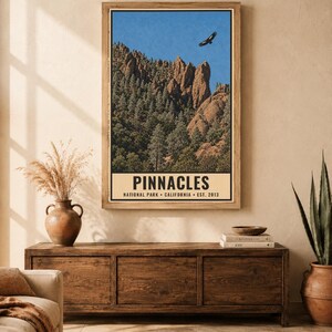 Op de afbeelding: Een verticale poster met een landschap van Pinnacles National Park met rotsachtige kliffen, dennenbomen en een vogel die in een blauwe lucht vliegt. Het onderste gedeelte heeft een cr&egrave;mekleurige rand met de tekst PINNACLES NATIONAL PARK CALIFORNIA EST. 2013.