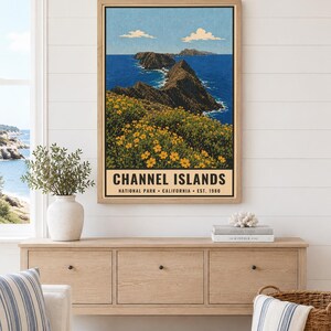 May include: A framed wall art print depicting a coastal landscape with yellow wildflowers in the foreground, rocky cliffs, and deep blue ocean water under a clear sky. The text reads CHANNEL ISLANDS NATIONAL PARK CALIFORNIA EST. 1980.