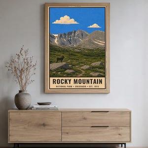 May include: A vertical rectangular wall art print featuring a landscape of Rocky Mountain National Park. The illustration shows a bighorn sheep on a rock, green meadows, and snow-capped mountains under a blue sky. Text reads ROCKY MOUNTAIN NATIONAL PARK COLORADO EST. 1915.