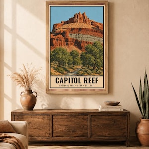 May include: A vertical wall art print featuring a landscape illustration of Capitol Reef National Park in Utah. The image displays red rock cliffs, green trees, and a stream under a blue sky, with the text CAPITOL REEF NATIONAL PARK UTAH EST. 1971.
