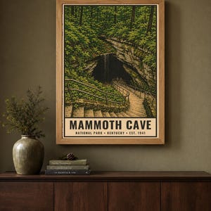 May include: A framed vertical poster featuring a detailed illustration of the Mammoth Cave entrance in Kentucky, with stone stairs, metal railings, and lush green forest foliage. The text reads MAMMOTH CAVE NATIONAL PARK KENTUCKY EST. 1941.