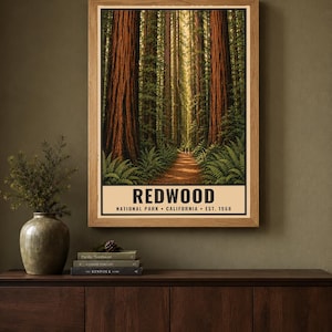 May include: A vertical rectangular poster in a light wood frame featuring a forest scene with tall redwood trees, green ferns, and a dirt path. The text at the bottom reads REDWOOD NATIONAL PARK &bull; CALIFORNIA &bull; EST. 1968 in black capital letters.