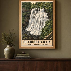 Może przedstawiać: Oprawiony wydruk ścienny przedstawiający wodospad w Parku Narodowym Cuyahoga Valley w Ohio, założonym w 2000 roku. Ilustracja ukazuje kaskadę wodną otoczoną zielonymi drzewami, skalistymi klifami i drewnianą barierką w jasnej drewnianej ramie.
