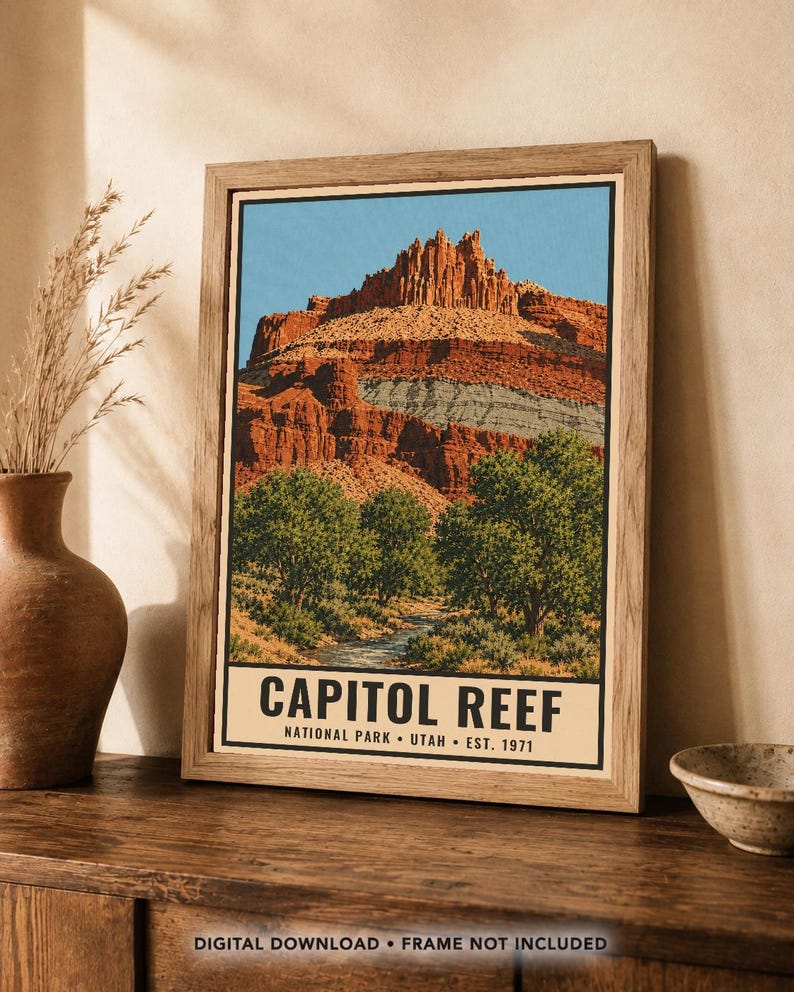 May include: A framed poster featuring a landscape illustration of Capitol Reef National Park in Utah. The artwork displays red rock cliffs, green trees, and a stream under a blue sky. The text reads CAPITOL REEF NATIONAL PARK UTAH EST. 1971.