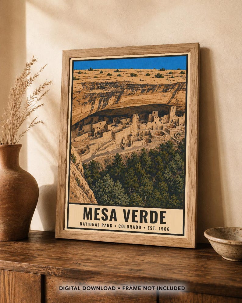 Pu&ograve; includere: Una stampa incorniciata con un'illustrazione paesaggistica del Mesa Verde National Park in Colorado. L'opera raffigura abitazioni rupestri sotto una sporgenza rocciosa, con un cielo blu brillante e alberi verdi. Il testo recita MESA VERDE.