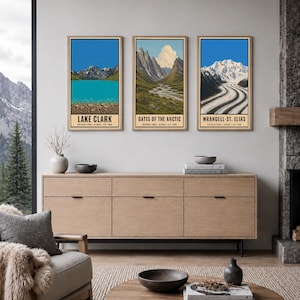 Pu&ograve; includere: Tre stampe artistiche verticali in cornici di legno chiaro appese a una parete. Le stampe raffigurano i parchi nazionali di Lake Clark, Gates of the Arctic e Wrangell-St. Elias in Alaska, con paesaggi montani, ghiacciai e fiumi.