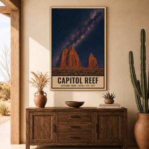 May include: A vertical wall art print featuring a night sky with a visible Milky Way galaxy above the red rock formations of Capitol Reef National Park. The text at the bottom reads CAPITOL REEF NATIONAL PARK UTAH EST. 1971 in a bold font.